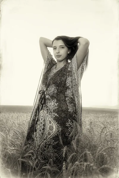 Jeune femme souriante avec robe ornementale debout sur un champ de blé avec coucher de soleil. Image vintage . — Photo