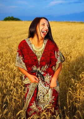 Gülümseyen gün batımı ile buğday alan üzerinde duran süs elbise ile genç kadın. Doğal arka plan..