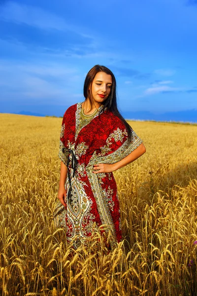 Leende ung kvinna med prydnads klänning stående på en vete — Stockfoto
