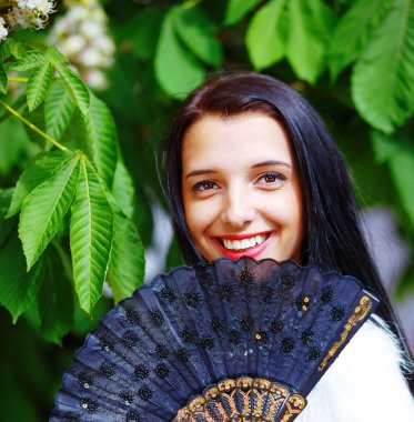 Smiling young woman smelling a beautiful sakura blossom, purple flowers. Spring Magic, and beautiful ornamental fan. Flower background.