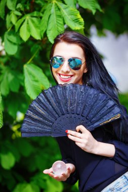Smiling young woman smelling a beautiful sakura blossom, purple flowers. Spring Magic, Magical Glass sphere in hand and beautiful ornamental fan. Flower background.
