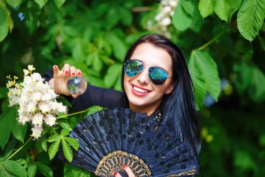Young woman smelling a bYoung woman smelling a beautiful sakura blossom, purple flowers. Spring Magic, Magical Glass sphere in hand and beautiful ornamental fan. Flower background.