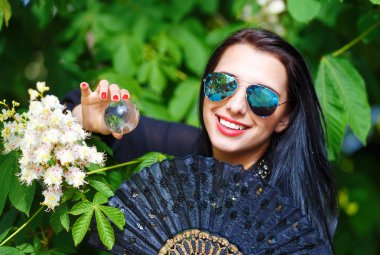 Young woman smelling a bYoung woman smelling a beautiful sakura blossom, purple flowers. Spring Magic, Magical Glass sphere in hand and beautiful ornamental fan. Flower background.