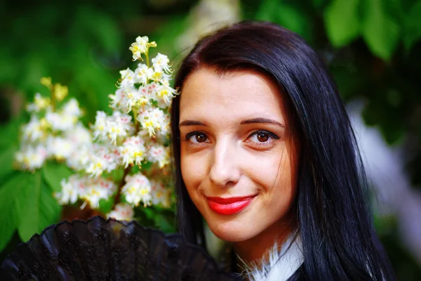 Mujer joven sonriente oliendo una hermosa magia de primavera, y un hermoso abanico ornamental y piel blanca. Fondo de flores . —  Fotos de Stock