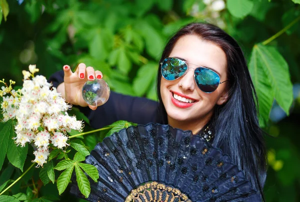 Young woman smelling a bYoung woman smelling a beautiful sakura blossom, purple flowers. Spring Magic, Magical Glass sphere in hand and beautiful ornamental fan. Flower background. — Stock Photo, Image