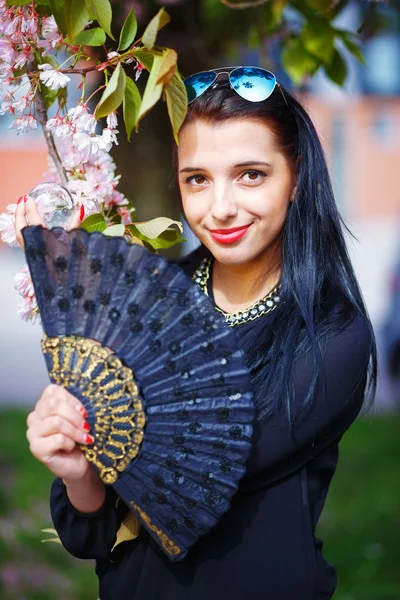 Young woman smelling a beautiful sakura blossom, purple flowers. Spring Magic, Magical Glass sphere in hand and beautiful ornamental fan — Stock Photo, Image