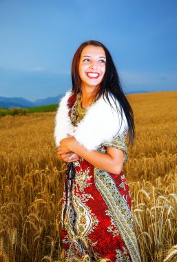 Gülümseyen gün batımı ile buğday alan üzerinde duran süs elbise ile genç kadın. Doğal arka plan