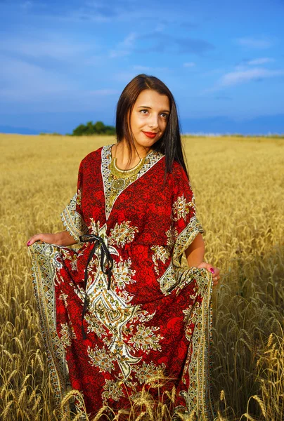 Улыбающаяся молодая женщина в декоративном платье, стоящая на пшеничном поле с закатом. Естественный фон — стоковое фото