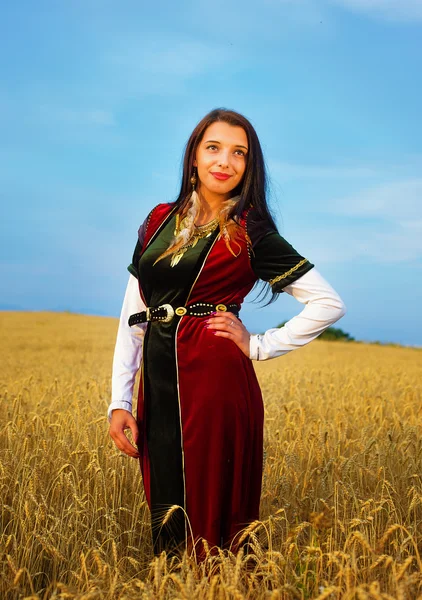 Jeune femme souriante avec robe ornementale debout sur un champ de blé avec coucher de soleil. Contexte naturel — Photo