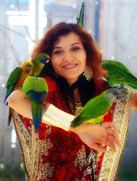 Jonge vrouw in decoratieve jurk en prachtige gouden sieraden en juwelen met een kleur papegaaien — Stockfoto