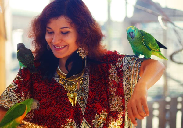 Mujer joven en vestido ornamental y hermosas joyas de oro con loros de color —  Fotos de Stock