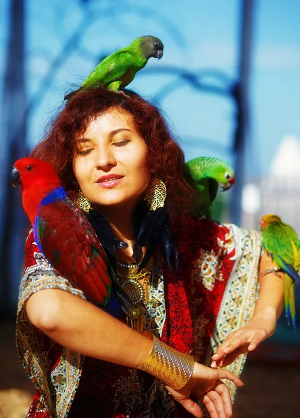 Mujer joven en vestido ornamental y hermosas joyas de oro con loros de color —  Fotos de Stock