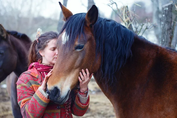 Mujer retrato y caballo en el exterior. mujer abrazando a un caballo y tiene plumas en el pelo — Foto de Stock