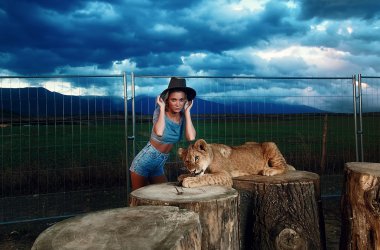 sexy woman playing with lion cub on background with beautiful sky and storm clouds.