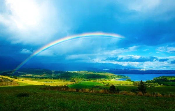 Beau paysage, prairie verte et jaune et lac avec montagne en arrière-plan avec un arc-en-ciel dans le ciel — Photo