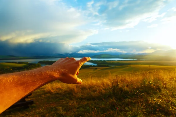 Beautiful landscape, green and yellow meadow and lake with mountain in background. with man hand at the sun. — Stock Fotó