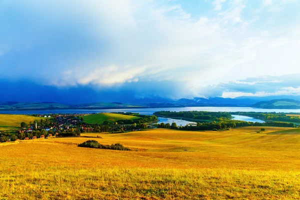 Prachtig landschap, groene en gele weide en meer met dorpje. Slowakije, Midden-Europa. — Stockfoto