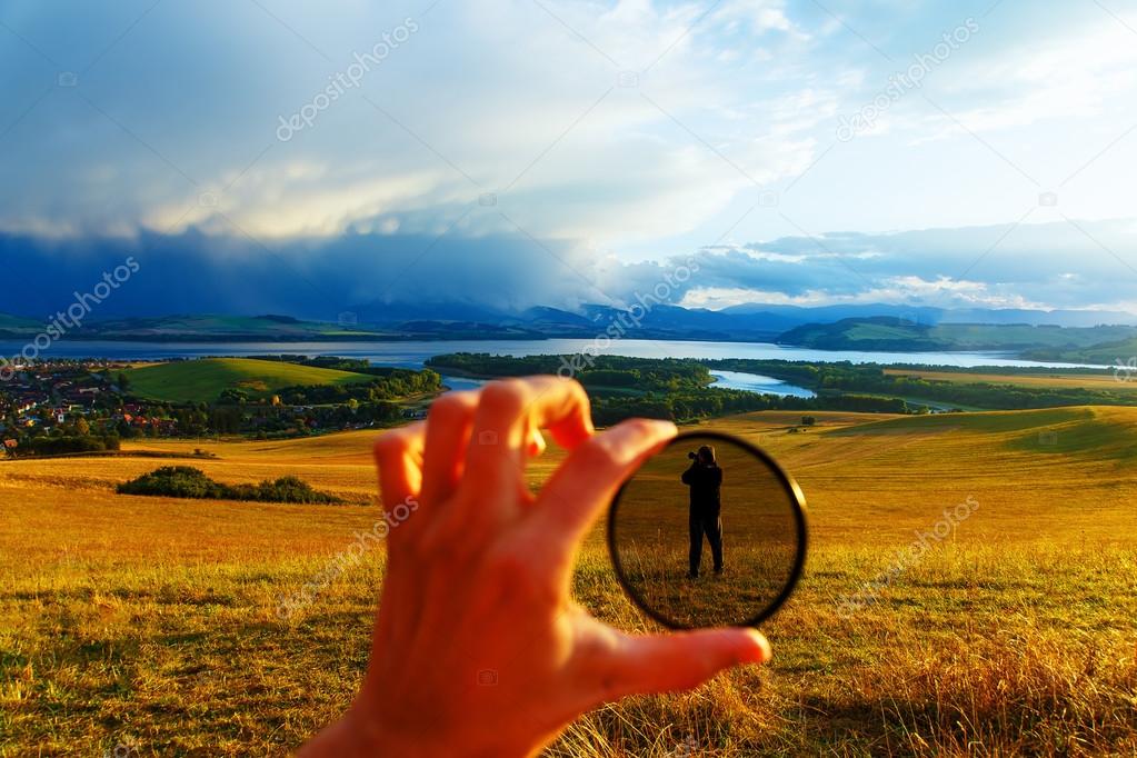 Beautiful landscape, green and yellow meadow and lake with mountain in background. People in polarization filter in man hand.