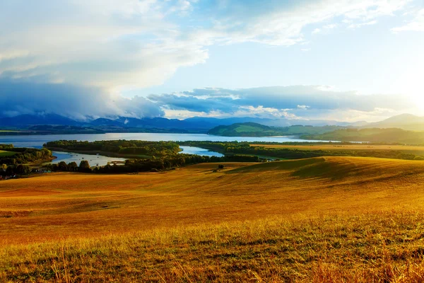 Krásná krajina, zelená a žlutá louka a jezero s horou v pozadí. Slovensko, střední Evropa. — Stock fotografie