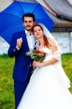 Gelin ve damat bir tarihi kilise mavi şemsiye ile.