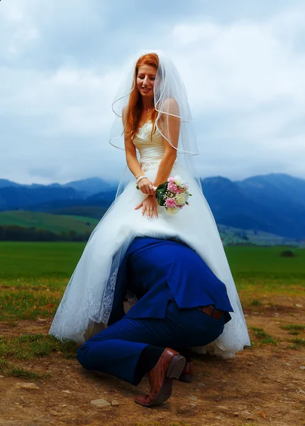 Bräutigam lugt unter Brautkleid - lustiges Hochzeitskonzept. — Stockfoto