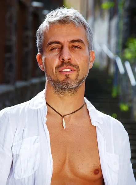 Sexy modelo masculino retrato de moda caliente en jeans elegantes y camisa con cuerpo muscular posando. Colgante de joyas de dientes de lobos —  Fotos de Stock