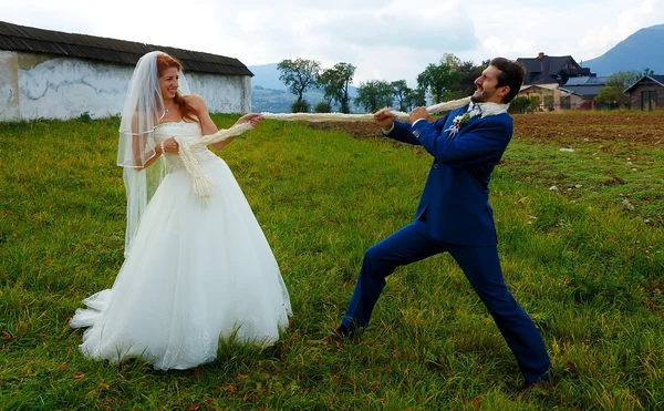 Braut zieht ihren Bräutigam mit Seil zu sich - lustiges Hochzeitskonzept. — Stockfoto