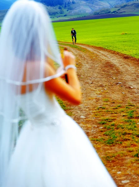 Braut mit Bierflasche und Bräutigam auf Fahrrad im Hintergrund - Hochzeitskonzept. — Stockfoto