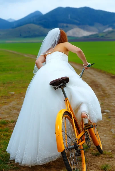 Braut auf orangefarbenem Fahrrad in wunderschönem Brautkleid mit Spitze in der Landschaft. Hochzeitskonzept. — Stockfoto