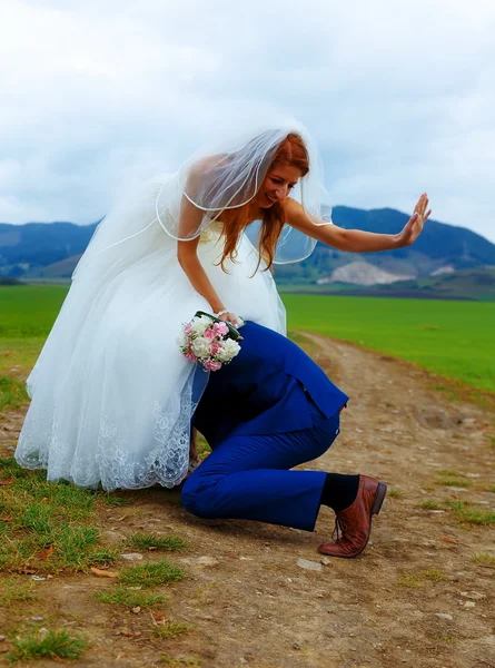 Bräutigam lugt unter Brautkleid - lustiges Hochzeitskonzept. — Stockfoto