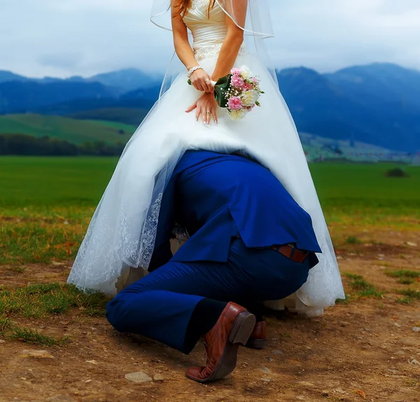 Noivo espreitando sob seu vestido de noiva conceito de casamento engraçado . — Fotografia de Stock