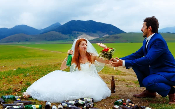 Betrunkene Braut mit vielen leeren Bierflaschen in Berglandschaft und Bräutigam kommen zu ihr - lustiges Hochzeitskonzept. — Stockfoto