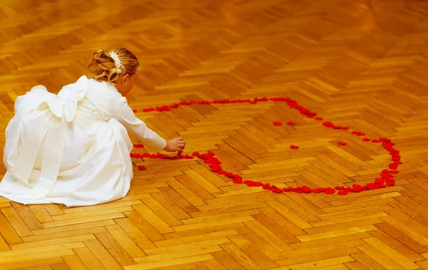 Little bridesmaid girl in white dress forming a heart shape out of rose petals.  wedding concept. — Stock Photo, Image