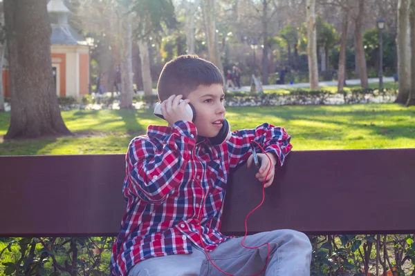 音楽を聞きながらベンチに座って公園の少年 — ストック写真
