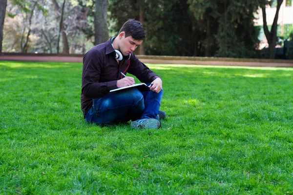 Le gars sur l'herbe écrit dans un cahier — Photo