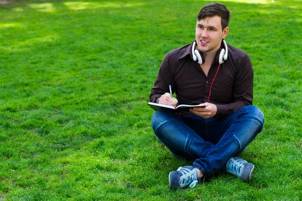 Chlap na trávě píše v poznámkovém bloku — Stock fotografie