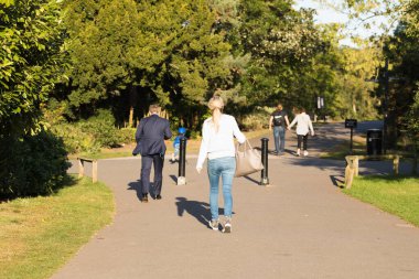 Güneşli bir günde, Yeşil Ağaçlar Arasında Asfalt Yolu boyunca Farklı Yoldan Geçenler Yürüyüşü. İngiliz Parkı. Şehir Halkı Tarzı, Park Bölgesi, Sonbaharın Başları. Sağlıklı Yürüyüş Her gün.