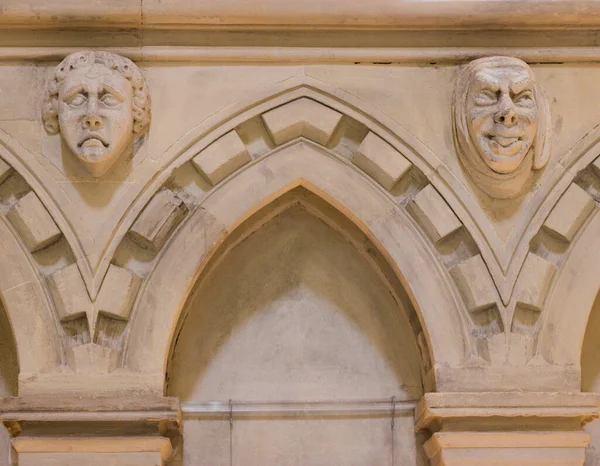 Eskiler 'in duvarlarla çevrili kapısı ve eski tasarım duvarındaki iki adamın garip yüz ifadesi. Tuhaf yüzler arasındaki eski kapalı giriş. İngiltere 'deki Tapınak Kilisesi' nin tuhaf iç mimarisi..