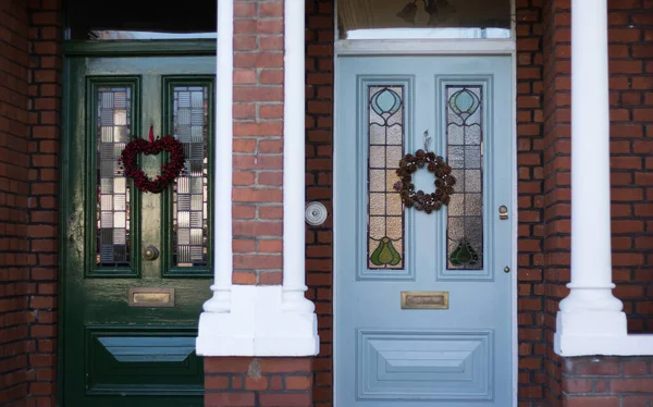 Geleneksel Noel çelenkleri olan iki güzel kapalı kapı. İngilizce yarı bağımsız stil. Noel hazırlığı ve komşu mahallede yaşamak..