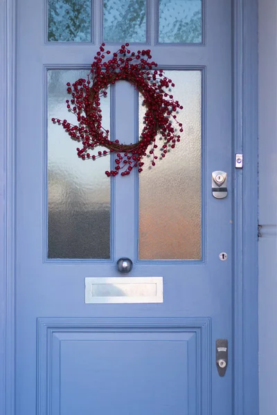 Dikey Resim. Kırmızı Çelenk Dekorasyonu ve Posta Kutusu ile Güzel Mavi Ön Kapı. İngiliz mimari tarzı. Noel ve Yeni Yıl Geleneksel Dekorasyonu Ev Dışı. Dikey Görüntü.