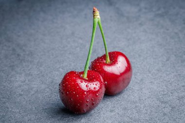 Yeşil saplı iki kırmızı kiraz küçük su sıçramaları ile kaplı koyu gri arka plan, yumuşak yansımalı üst manzara