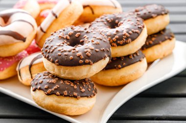 Kahverengi çikolatalı donutlar, beyaz bir tabakta kahverengi serpiştirilmiş siyah bir masada yumuşak ve hafif bir durumda, tipik Amerikan sağlıksız fast food.