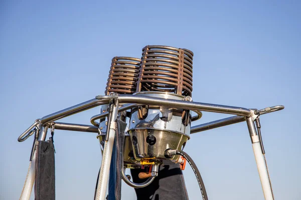 Close-up of a hot air balloon gas burner for propane gas, looking from the side, gas burner mounted onto basket, gas valves and pipes, blue sky background