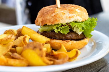 Tipik bir hamburger, köfte, çörek ve bir dilim salata. Tahta bir masada duran beyaz tabakta taze ve el yapımı alevler..