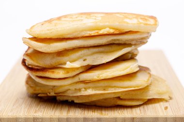 Üniformalı beyaz arka planda bambu kesme tahtasındaki krep yığınının yan görüntüsü. Kahvaltı için ev yemeği ya da fast food.