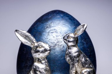 Mavi bir kraliyet yumurtası, yaratıcı Paskalya ve bahar dekorasyonu 2020 'nin önünde iki gümüş eş Paskalya figürünün yakın çekimi, beyaz izole arka planda moda renkleri