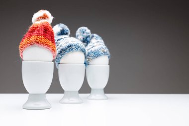 Koyu gri arka planda mavi ve turuncu bir bere takıp bir masaya yerleştirilmiş üç yumurta kabı Paskalya tebrik kartı ya da Noel tebrik kartı olarak kullanılabilir.