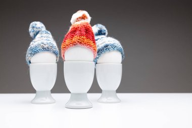 Beyaz yumurtalı ve yün boncuklu üç yumurta fincanı, beyaz bir masanın üzerinde koyu gri arka plan, Paskalya tebrik kartı veya Noel tebrik kartı olarak kullanılır..