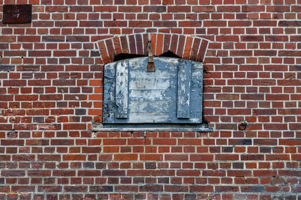Small window in a brick wall covered with a blue painted lid made of wood, weathered look and damaged brick wall, use as game asset or texture reference