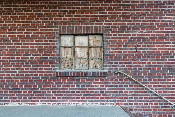 Broken window of a industrial building on a red brick wall, a wood board behind the broken glas to cover the holes, handrail and concrete floor, game asset texture or reference image